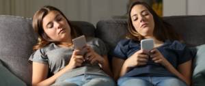 Deux adolescentes qui regardent leur smartphone allongées sur un canapé