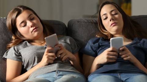 Deux adolescentes qui regardent leur smartphone allongées sur un canapé