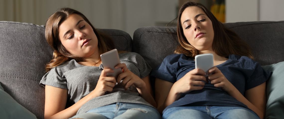Les jeunes n'agissent pas vraiment pour le climat Deux adolescentes qui regardent leur smartphone allongées sur un canapé