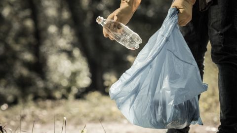 Que prévoit vraiment la loi anti-gaspi ?  Un homme en train de jeter une bouteille en plastique dans un sac poubelle