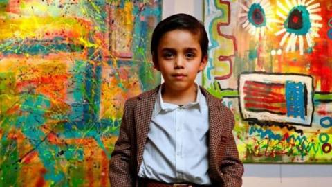 Un enfant artiste pose devant ses peintures