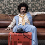 un homme moustachu regarde une télévision