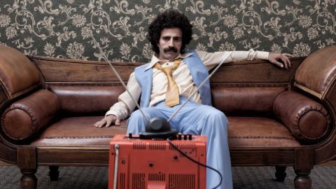 un homme moustachu regarde une télévision