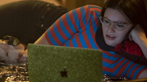 Une jeune fille brune allongée sur un lit devant un ordi