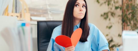 Comment trouver l'amour au travail ? Une femme dans un bureau en train de tenir un coeur rouge en papier