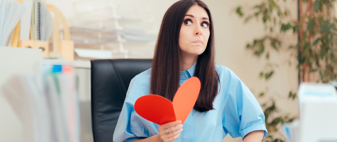Comment trouver l'amour au travail ? Une femme dans un bureau en train de tenir un coeur rouge en papier