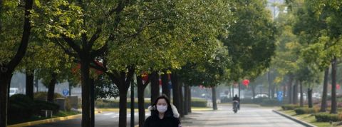 Le coronavirus fait baisser la pollution en Chine Une femme en Chine avec un masque sur le visage et des arbres autour