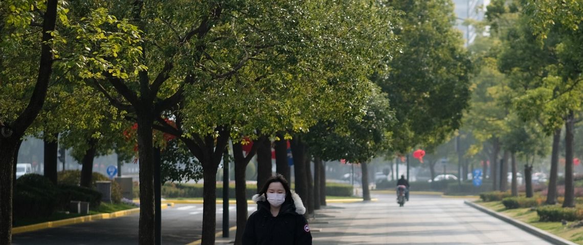 Le coronavirus fait baisser la pollution en Chine Une femme en Chine avec un masque sur le visage et des arbres autour