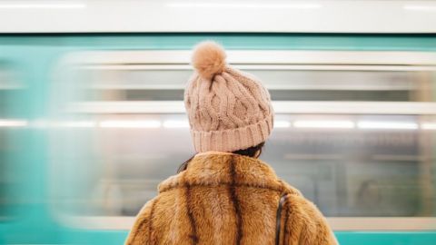 une fille en manteau de fourrure de dos face à un métro