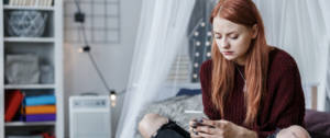 une adolescente sur son lit regarde son portable