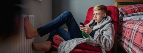 Les ados et leur smartphone un adolescent, pieds nus dans sa chambre avec un portable dans les mains.