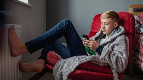 un adolescent, pieds nus dans sa chambre avec un portable dans les mains.