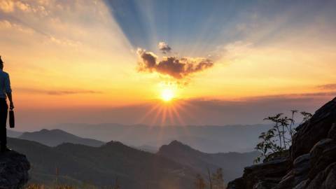 Un homme au sommet d'une montagne en train d'assister au lever du soleil