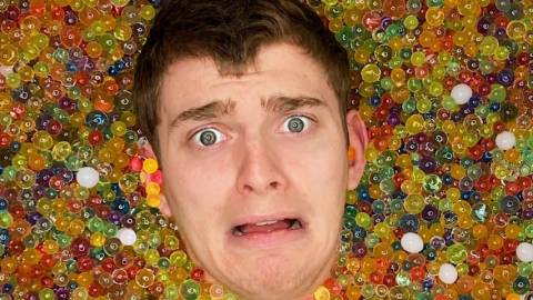 la tête d'un influenceur qui sort d'une baignoire pleine de billes colorées.