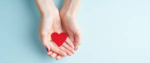 deux mains de femme tenant un coeur en papier rouge