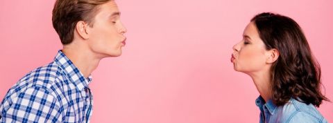 Comment draguer pendant l'épidémie de coronavirus ? Un homme et une femme qui se font un bisou à distance sur un fond rose