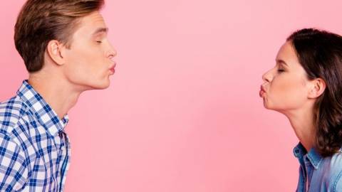 Un homme et une femme qui se font un bisou à distance sur un fond rose