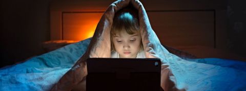 Comment gérer les écrans pendant le confinement ? Une petite fille qui joue sur un ordinateur cachée sous sa couette