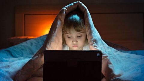 Une petite fille qui joue sur un ordinateur cachée sous sa couette