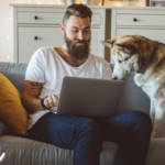 Un homme en train de travailler sur son canapé avec son chien