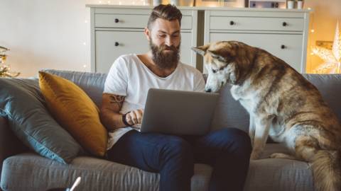 Un homme en train de travailler sur son canapé avec son chien