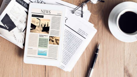 Des journaux posés sur une table avec une tasse de café et des lunettes