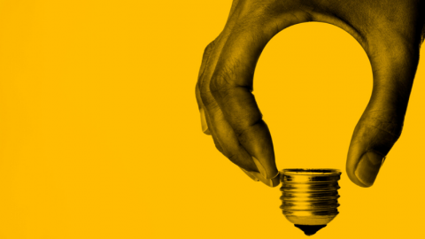 main qui tient une ampoule sur fond jaune