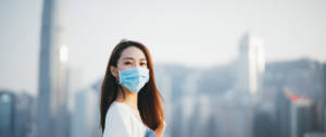 Une jeune femme asiatique, portant un masque de protection, regarde l'objectif sur fond de buildings