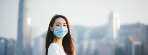Comment apprendre de l'Asie dans la crise du Coronavirus ? Une jeune femme asiatique, portant un masque de protection, regarde l'objectif sur fond de buildings