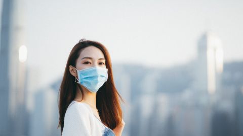 Une jeune femme asiatique, portant un masque de protection, regarde l'objectif sur fond de buildings