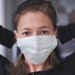 Une femme habillée en noir qui attache un masque chirurgical