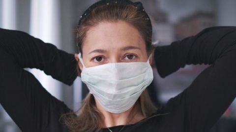 Une femme habillée en noir qui attache un masque chirurgical