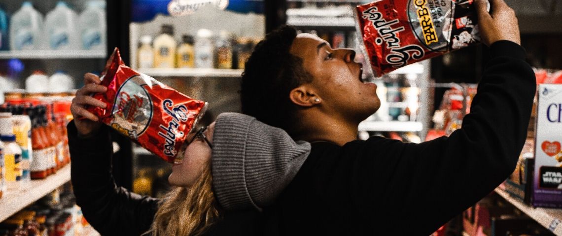 Comment le confinement modifie nos habitudes alimentaires Une femme et un homme qui mangent des chips dans un supermarché
