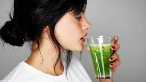 Une femme brune qui boit un jus vert