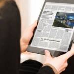 Une femme de dos qui lit le journal sur une tablette