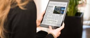 Une femme de dos qui lit le journal sur une tablette
