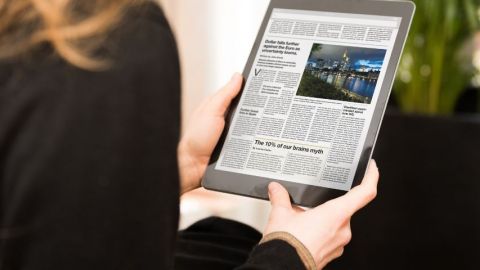 Une femme de dos qui lit le journal sur une tablette