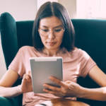 Une femme asiatique tenant une tablette dans un fauteuil vert