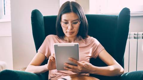 Une femme asiatique tenant une tablette dans un fauteuil vert