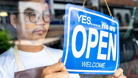 Un jeune homme portant des lunettes et un tablier ouvre sa boutique