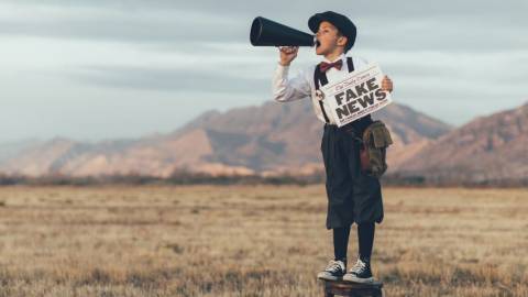 Un enfant avec un mégaphone et un journal où il est écrit Fake News