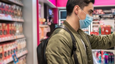 un homme portant un masque en train de faire ses courses au supermarché