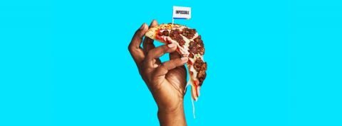 Les ventes de fausse viandes pendant la pandémie de Covid-19 Une main qui tient une pizza avec de la viande végétale sur un fond bleu