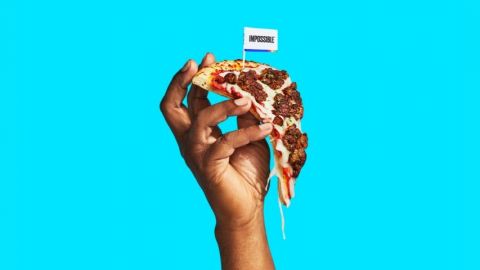 Une main qui tient une pizza avec de la viande végétale sur un fond bleu