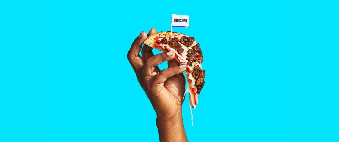 Les ventes de fausse viandes pendant la pandémie de Covid-19 Une main qui tient une pizza avec de la viande végétale sur un fond bleu