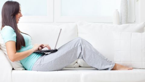 Une femme travaillant sur son canapé en jogging et pieds nus