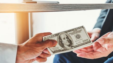 Main donnant un billet à une autre sous une table