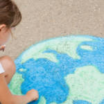 Une petite fille en train de dessiner une terre à la craie au sol