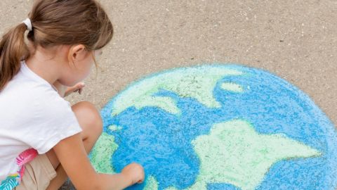 Une petite fille en train de dessiner une terre à la craie au sol
