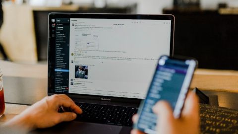 Personne en train de regarder son téléphone portable et Slack sur son ordinateur en simultané